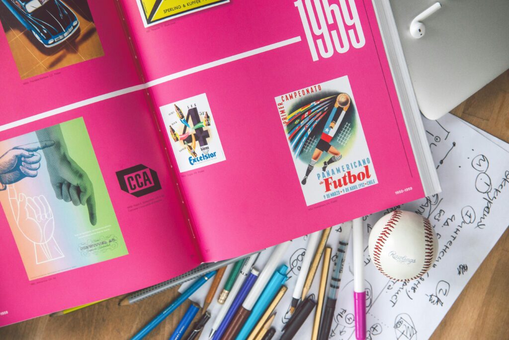 pexels-photo-3782129-3782129 Artistic workspace featuring an open design book, sketches, pens, and a baseball on a desk.