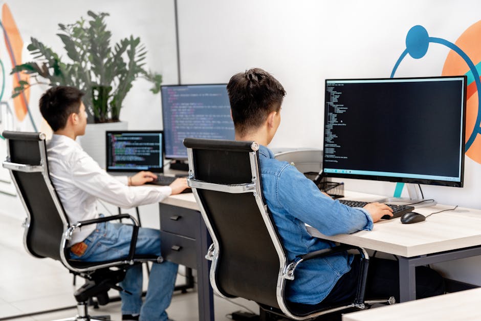 pexels-photo-7988079-7988079 Two male developers at desks programming in a modern office workspace with large monitors.